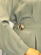 Green dress with a gold belt buckle on a neutral background