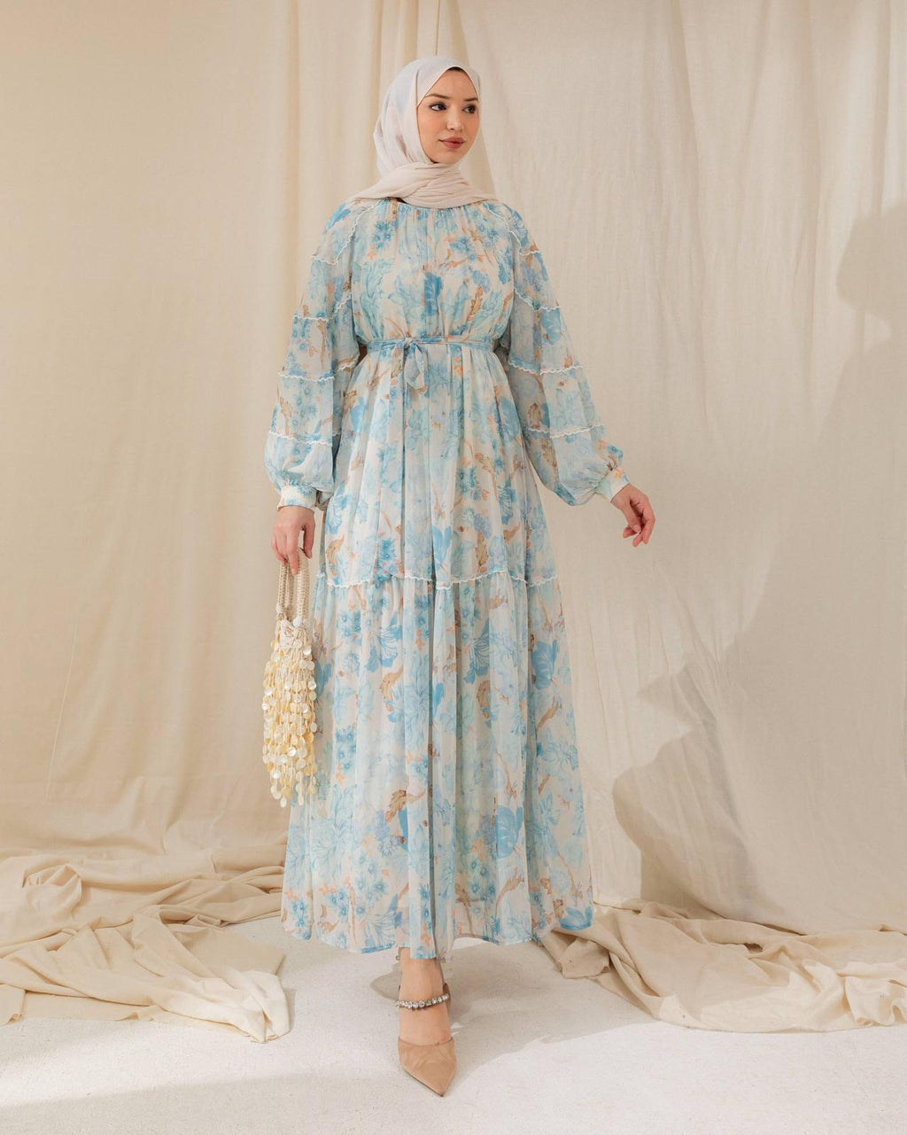 Woman wearing a floral dress and hijab against a plain background