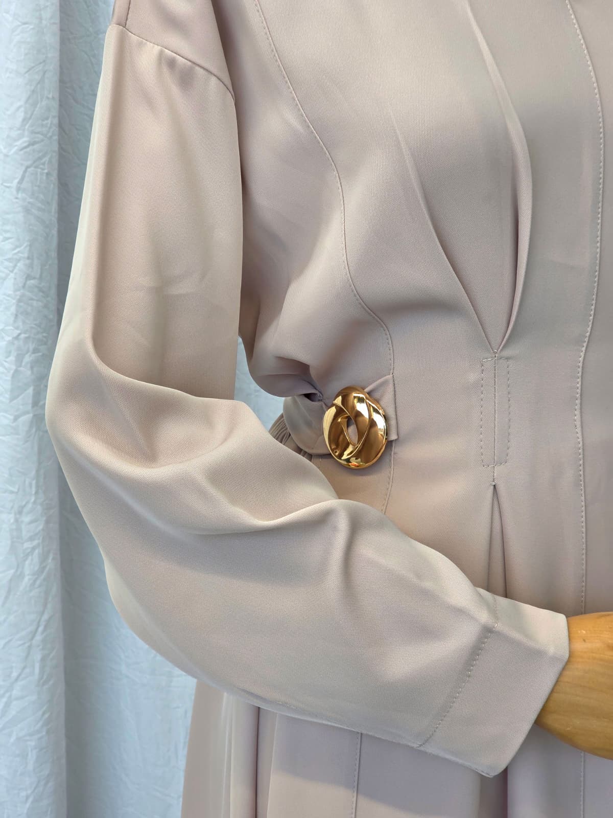Close-up of a beige dress with a gold button against a light blue background
