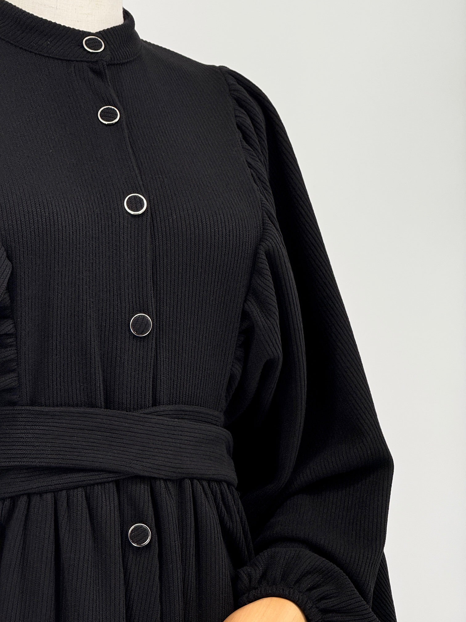 Close-up of a black ribbed knit dress with buttons and a belt on a white background