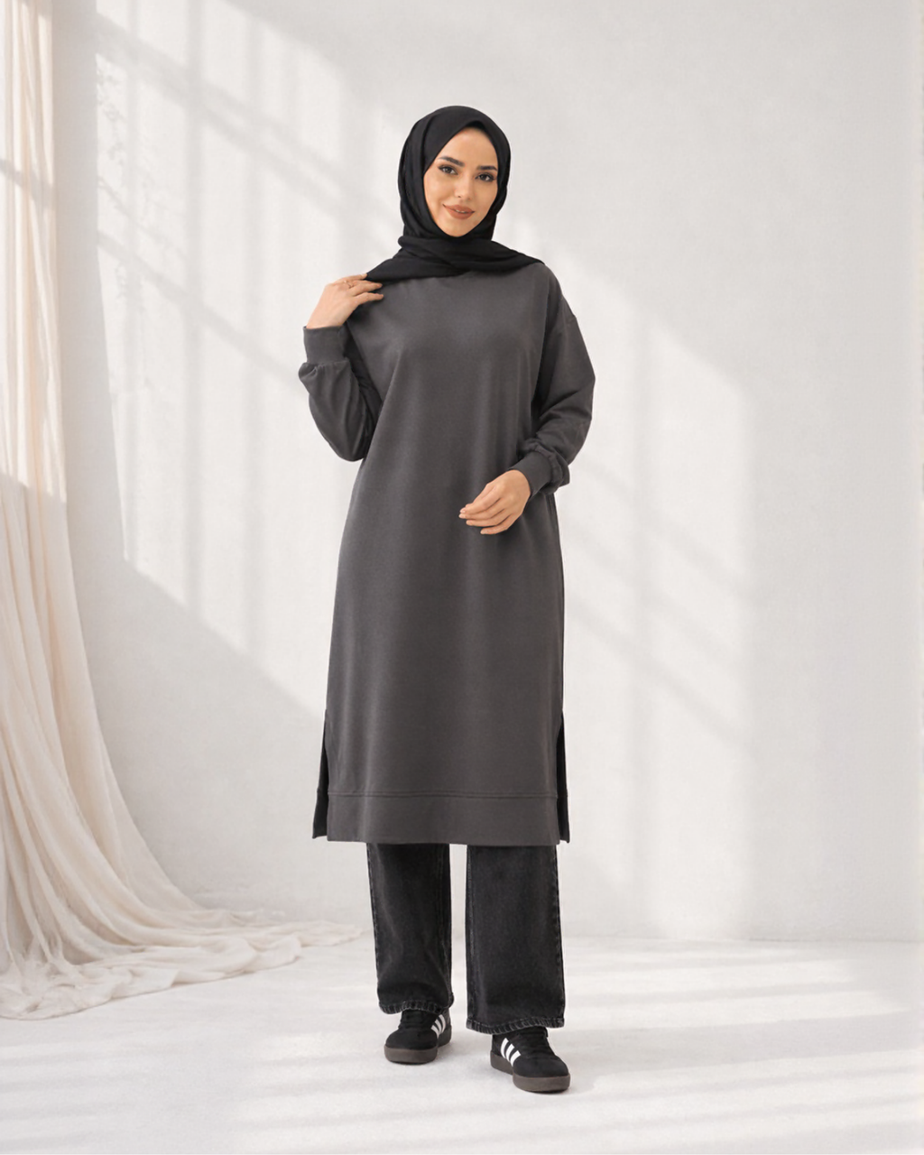 Woman wearing a long dark gray dress with a hood against a white background