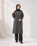 Woman wearing a long dark gray dress with a hood against a white background
