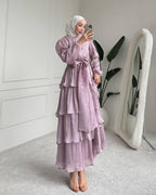 Woman in a light purple layered dress taking a mirror selfie in a minimalistic room.