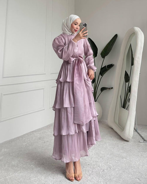 Woman in a light purple layered dress taking a mirror selfie in a minimalistic room.