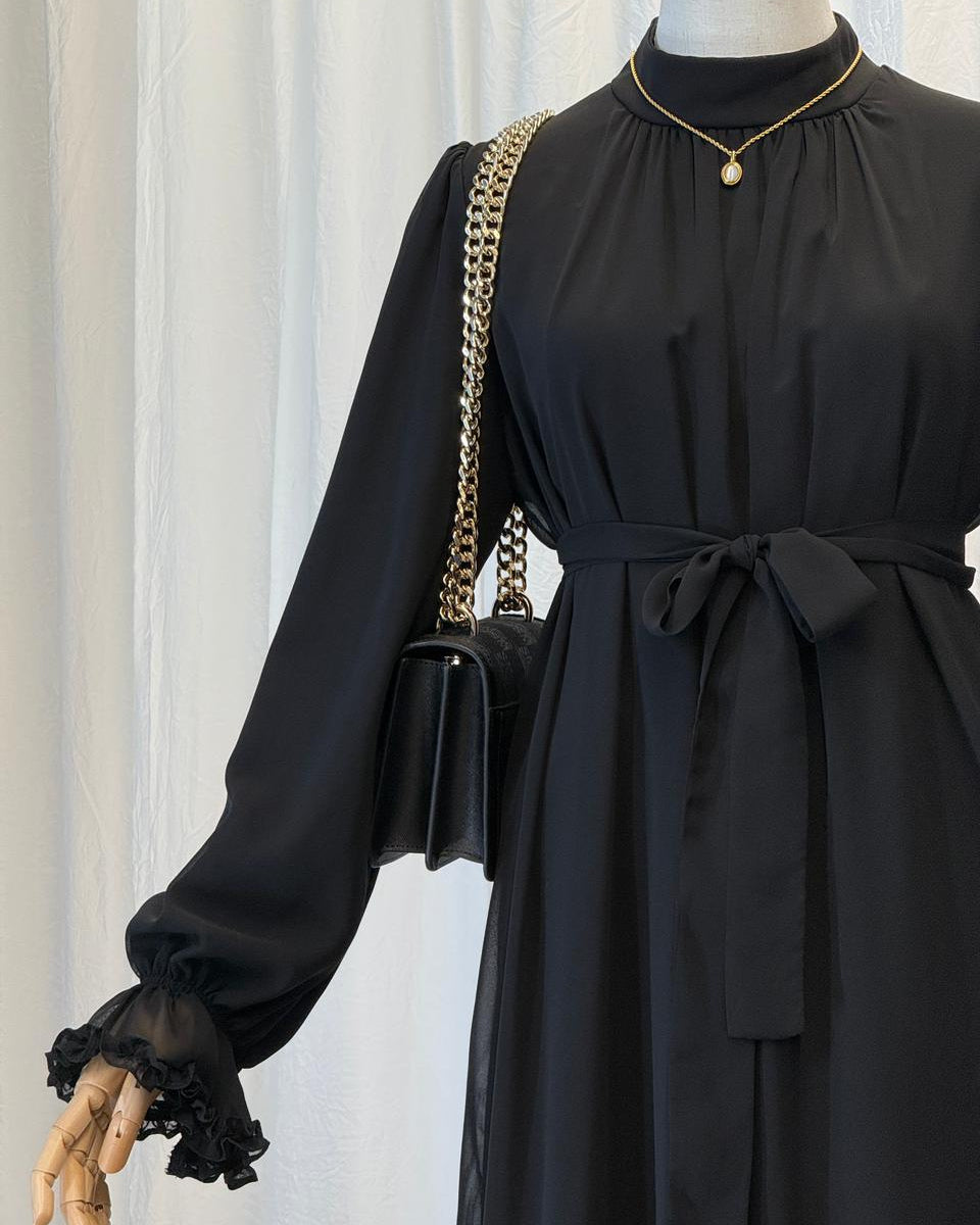 Mannequin wearing a black dress with a gold chain bag against a white curtain background