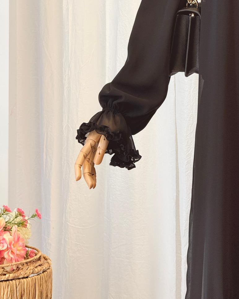 Black long-sleeve top with sheer sleeves on a neutral background