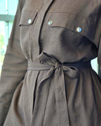Close-up of a brown linen shirt dress with a matching fabric tie belt, featuring two buttoned chest pockets and a textured weave.