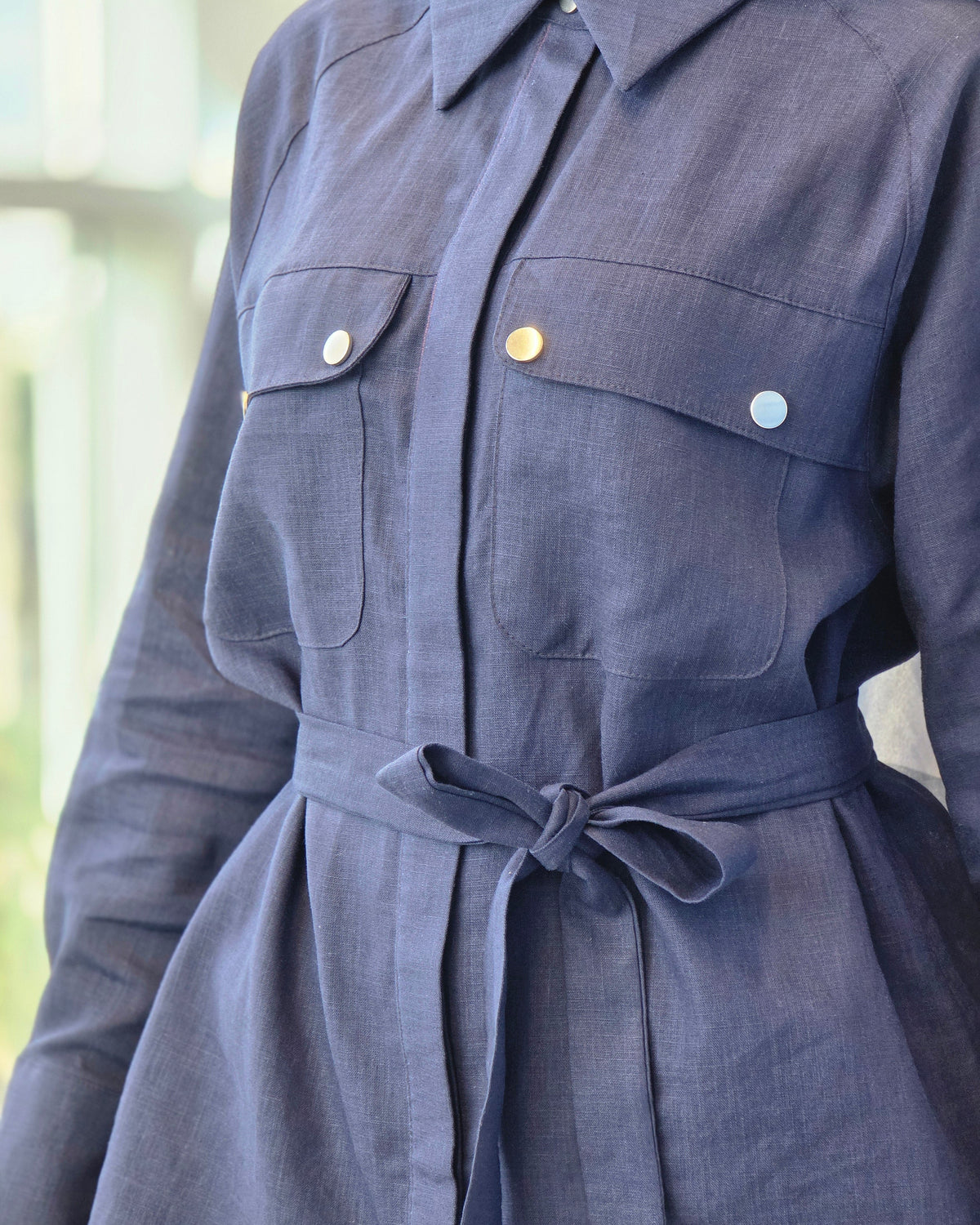 Close-up of a navy blue linen shirt dress with a tie waist belt and decorative buttons on the chest pockets.