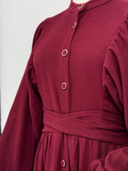 Close-up of a maroon ribbed knit dress with buttons and a belt on a white background