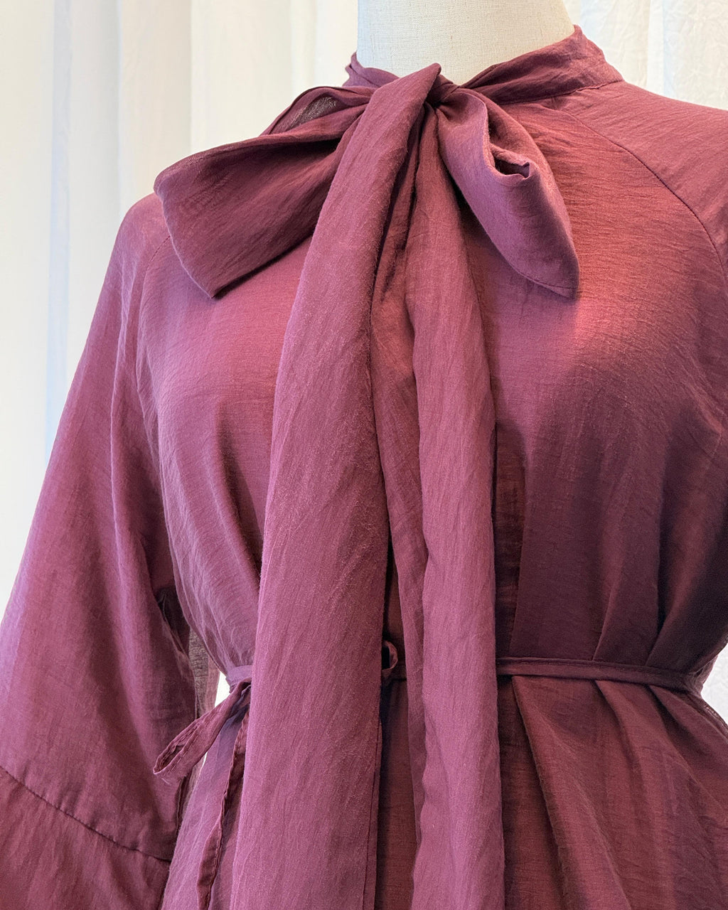 Mauve dress with a large bow on a mannequin against a white curtain background