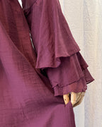 Close-up of a burgundy ruffled garment on a mannequin against a textured white wall.