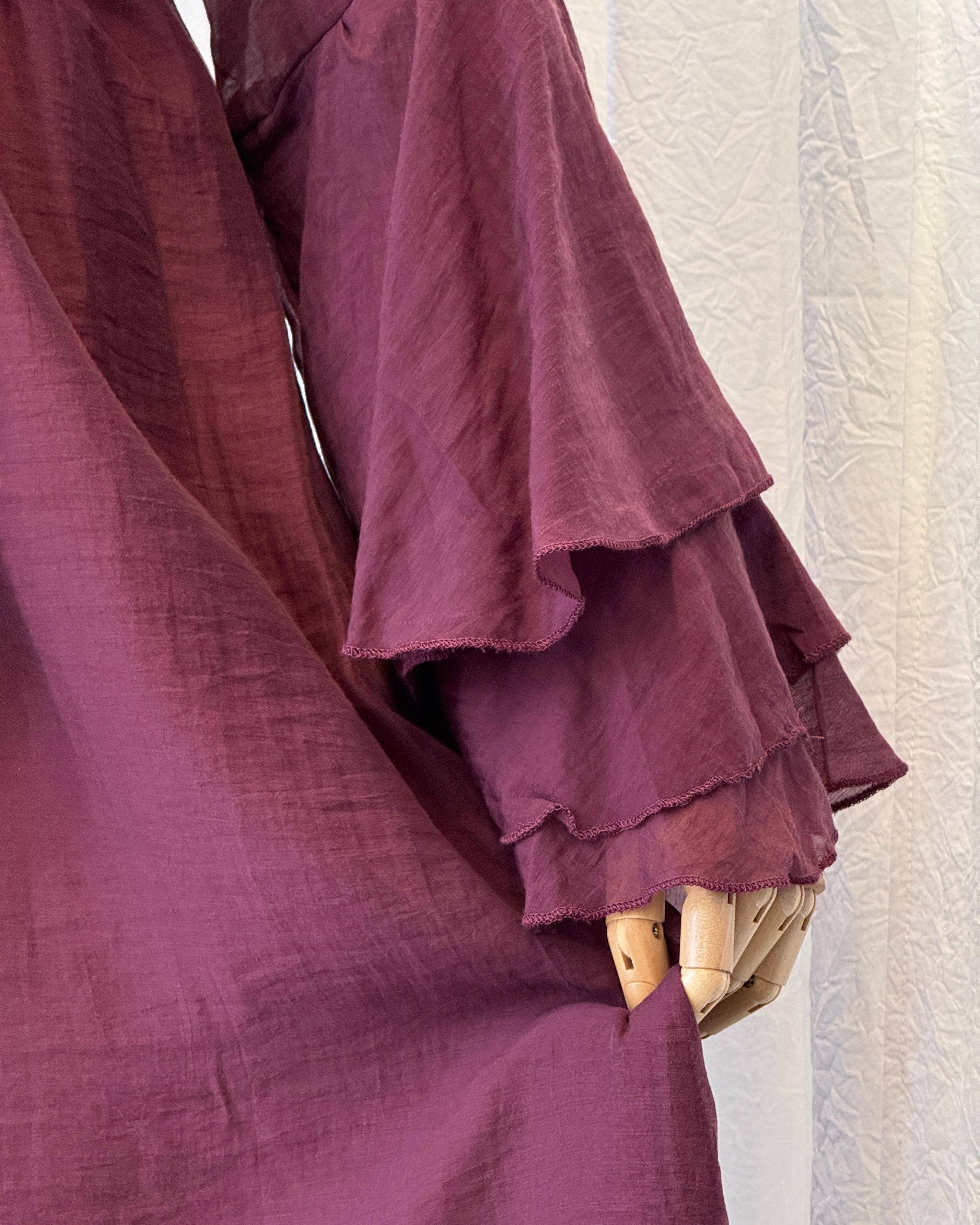 Close-up of a burgundy ruffled garment on a mannequin against a textured white wall.