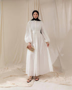 Woman wearing a white dress with long sleeves against a white curtain background