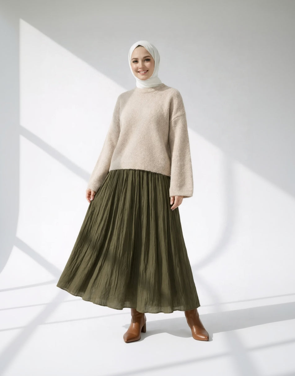 Woman wearing a beige sweater and olive green skirt on a white background