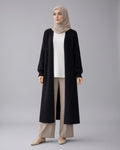 Woman wearing a black long cardigan, white top, beige hijab, and pants on a white background