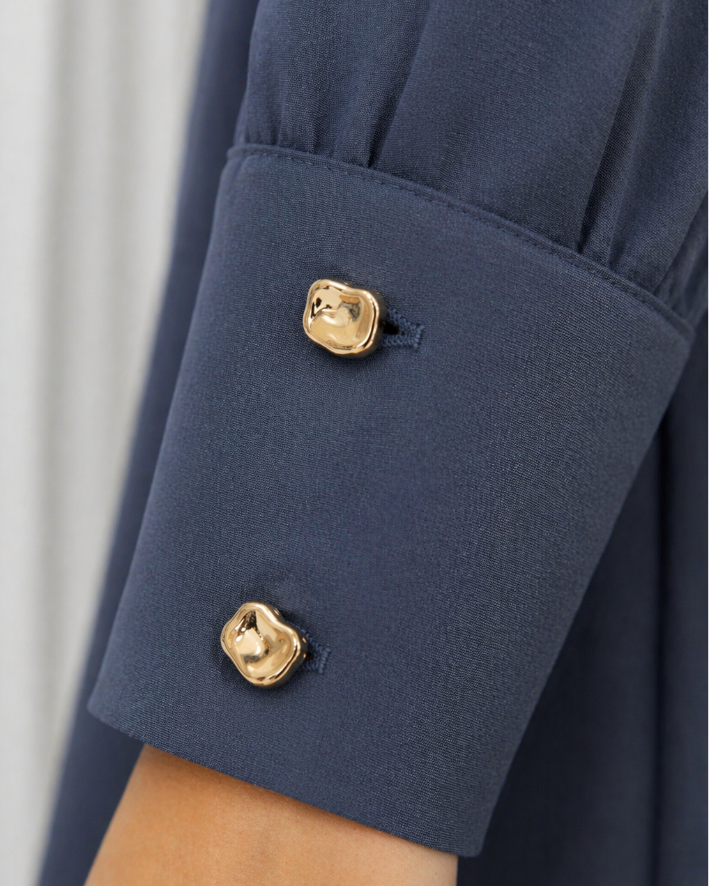 Navy blue sleeve with gold buttons on a blurred white background