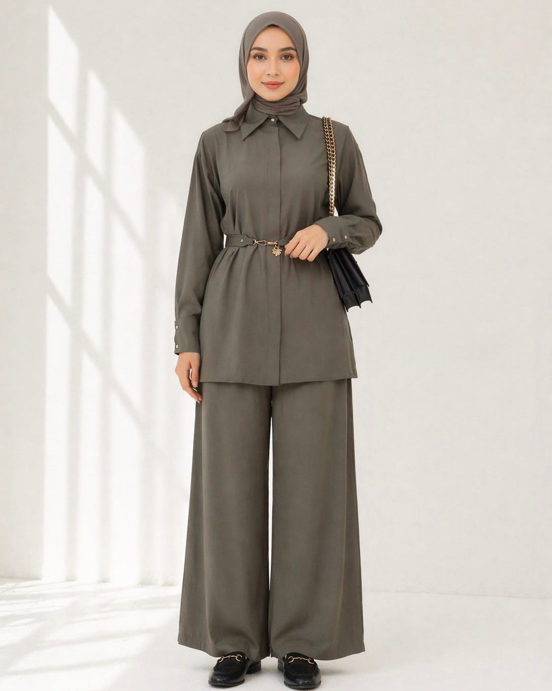 Woman wearing a dusty olive outfit with a hijab in a bright room.