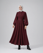 Woman wearing a burgundy dress with a white hijab on a gray background