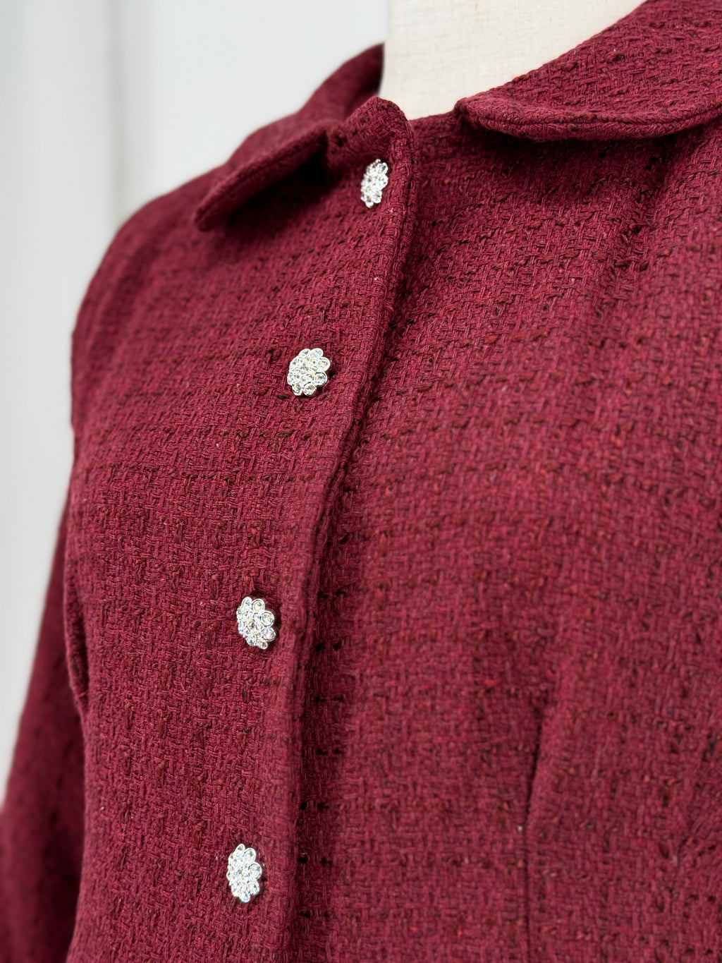 close-up of a burgundy tweed suit on a mannequin against a plain background