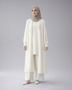 Woman wearing a white cardigan with a beige hijab in a minimalistic setting
